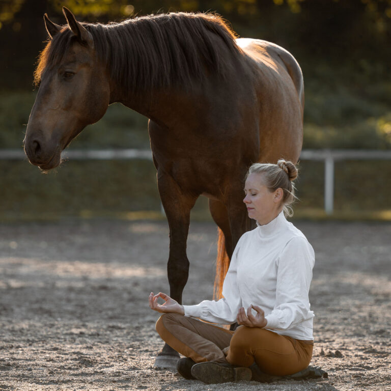 Lisa Jost sitzt in Meditationshaltung vor ihrem Pferd Letrado